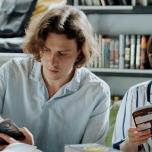 Two people reading books at a table in a cozy room with a bookshelf behind them.