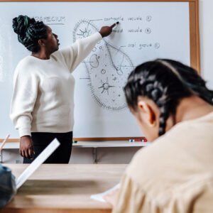 Black female teacher explains a biology diagram on a whiteboard to students in a classroom.