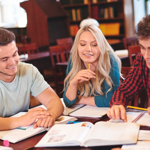 Group of four students studying together at a table with notebooks and an open textbook."